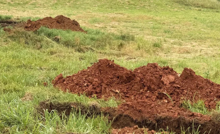 A rural landscape with a long trench dug through green grass and brown dirt mounds, leading to a silo.
